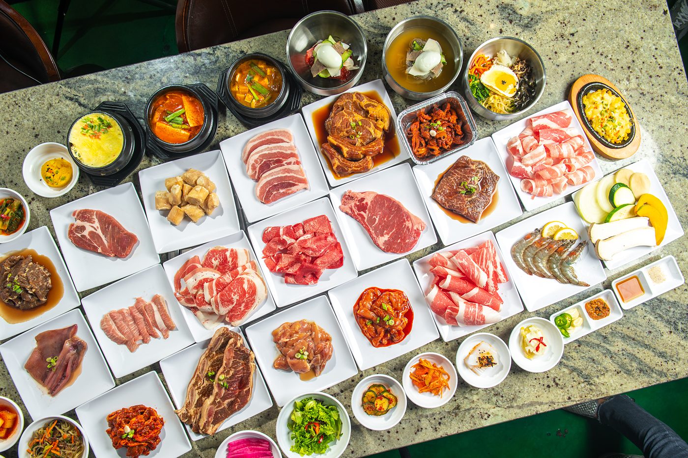 Full spread of AYCE meats, stews and banchan on a table